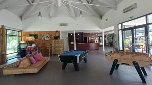 A spacious indoor area with a pool table, foosball table, and a seating area with a sofa and bar stools.