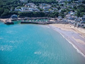 An aerial view of a coastal town with a marina, sandy beach, and residential buildings.