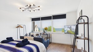A bedroom with a bed, a chair, a table, a TV, and a view of the sea. - Swn Y Mor - 1 Bedroom Studio - Saundersfoot (Saundersfoot)