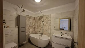 Een moderne badkamer met een vrijstaand bad, toilet, wastafel met spiegel en douche.