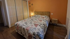 Een slaapkamer met een bed, houten vloer, oranje wanden en een schuifdeur.