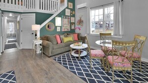 A spacious living room with a high ceiling, a staircase, a cozy sofa, a dining table with chairs, and a patterned rug. - Charming, quiet, sun filled, lakefront  (Willis)