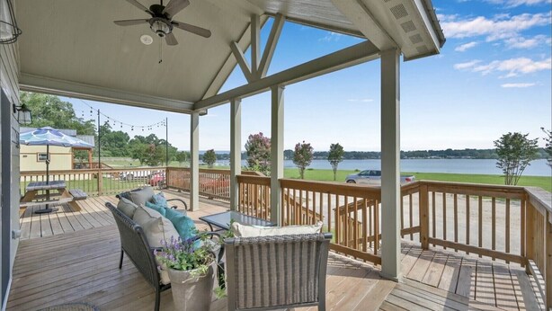 A covered deck with a ceiling fan, wicker furniture, and a view of a lake. - Charming, quiet, sun filled, lakefront  (Willis)