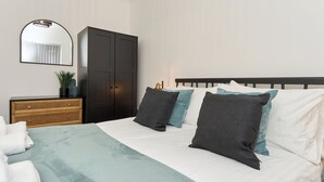 Ein ordentlich eingerichtetes Schlafzimmer mit einem Bett, einem Kleiderschrank, einem Spiegel und einem Nachttisch mit einer Lampe.