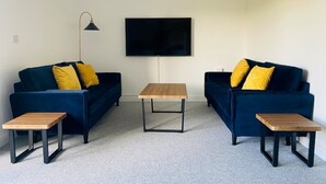 Un salon avec deux canapés bleu foncé, chacun agrémenté d’un coussin jaune, une table basse en bois et un lampadaire.