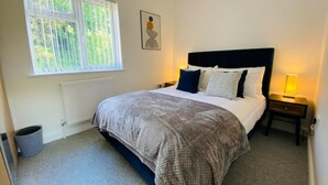 Une chambre à coucher avec un lit, une fenêtre, un radiateur, un tableau accroché au mur et une table de chevet avec une lampe.