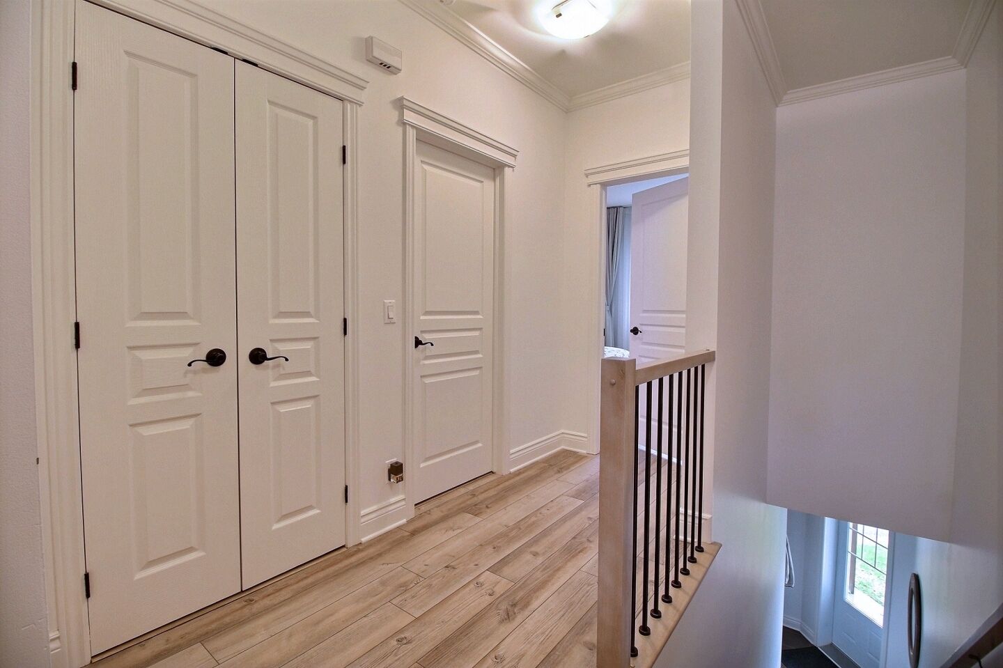 A hallway with white double doors, a wooden floor, and a staircase with a black railing.