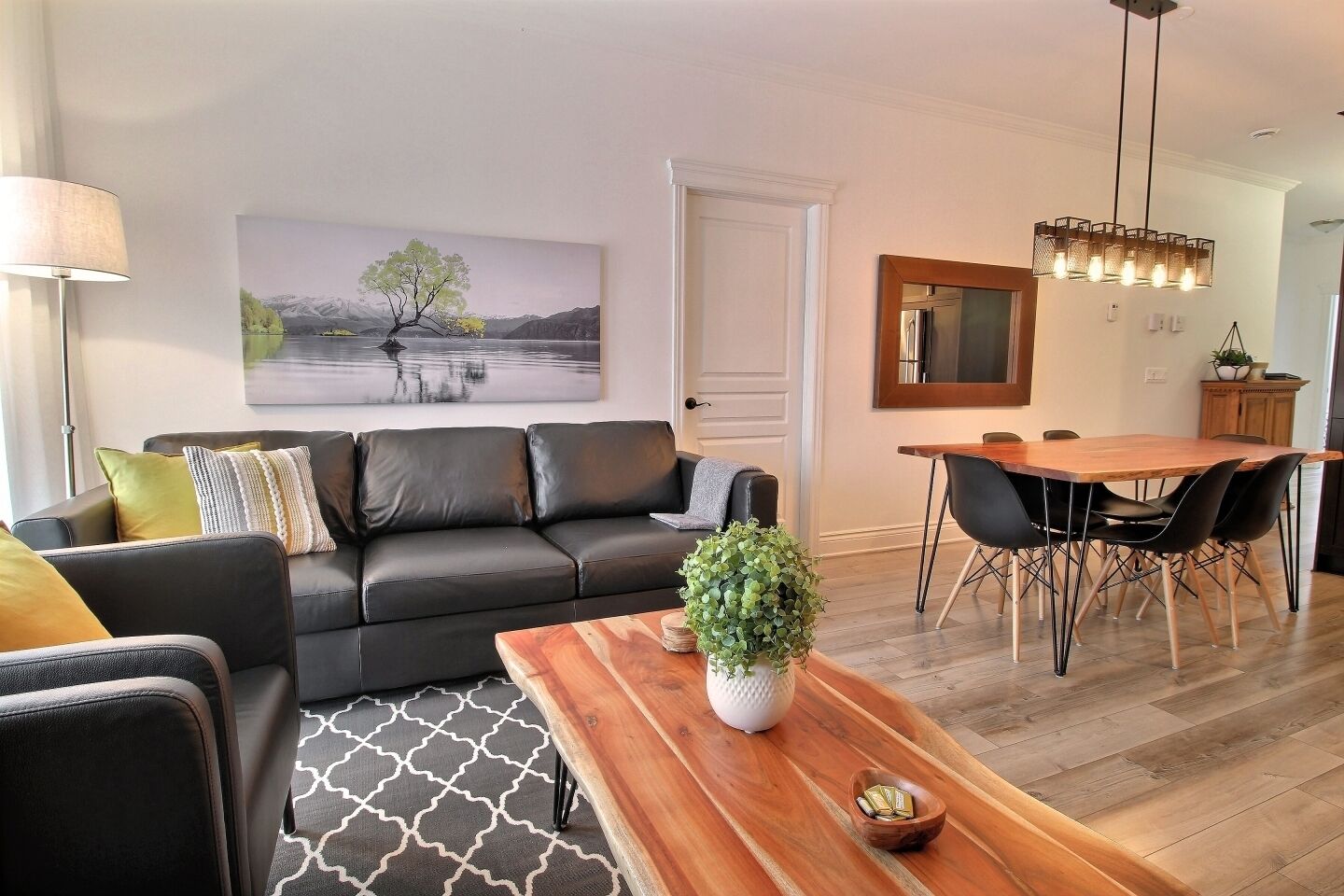 A modern living room with a black leather sofa, a wooden coffee table, and a dining area with a wooden table and chairs.