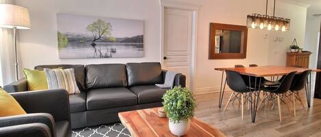 A modern living room with a black leather sofa, a wooden coffee table, and a dining area with a wooden table and chairs.