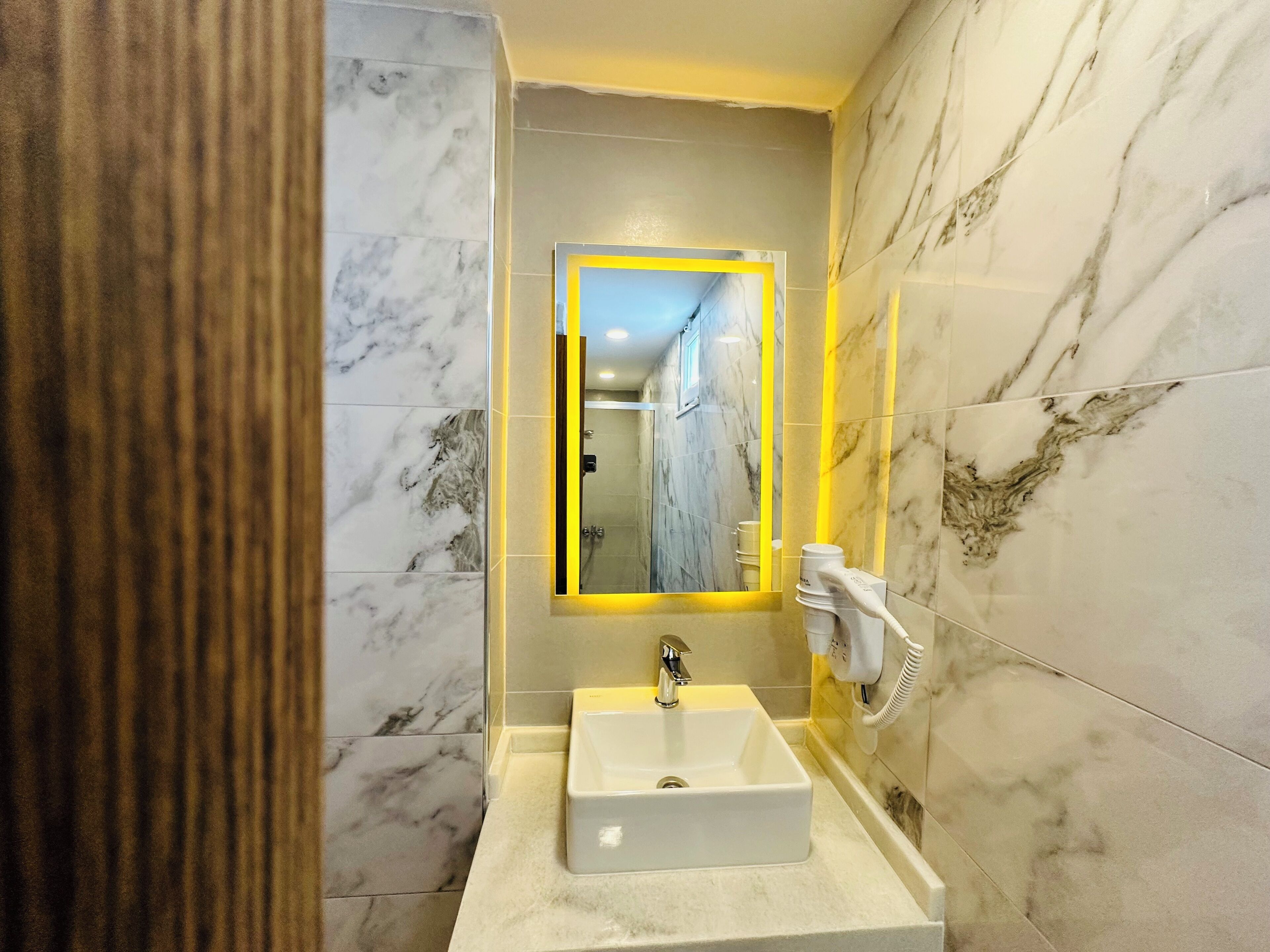 Un baño moderno con un lavabo de mármol, un espejo con marco amarillo y un secador de manos.