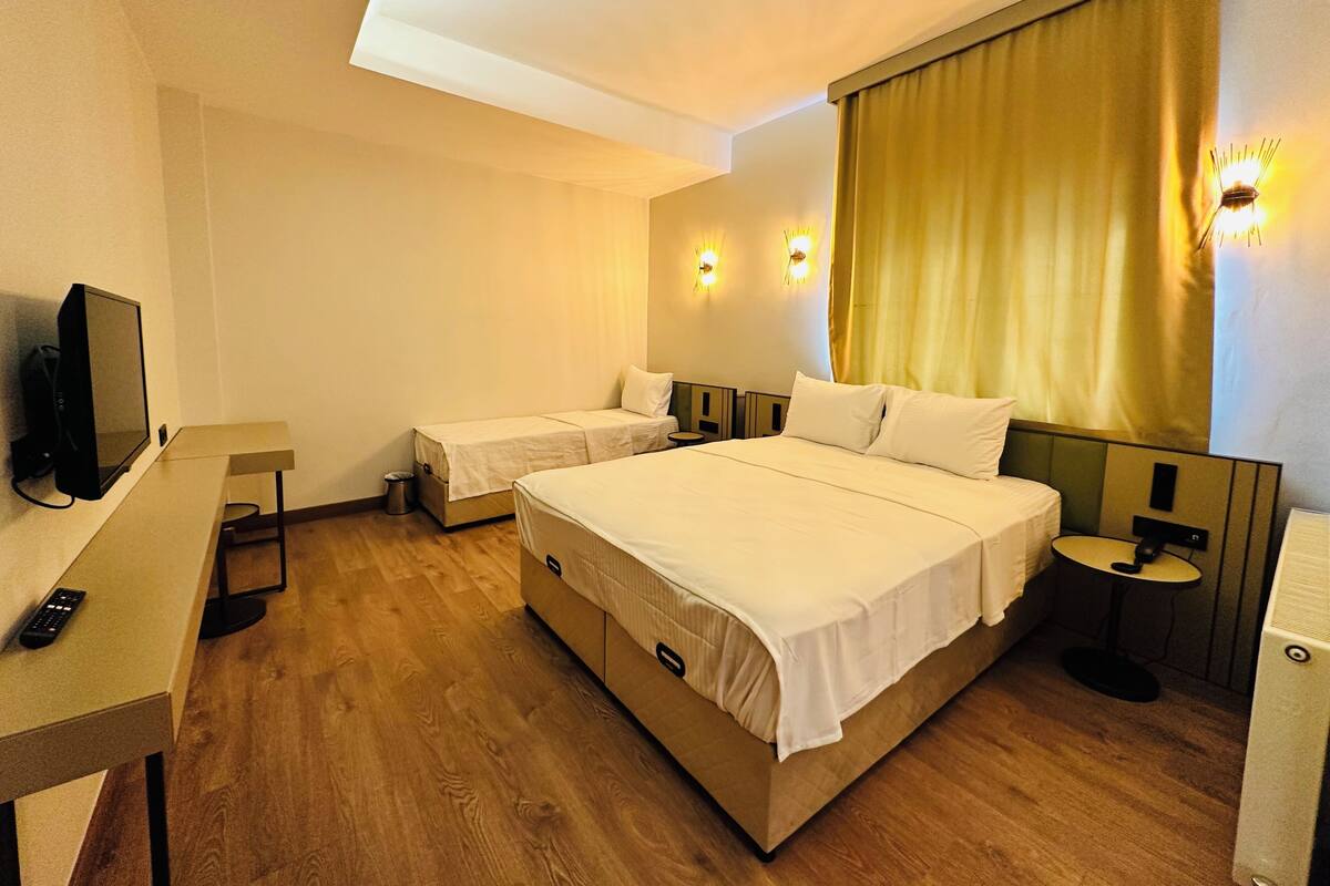 A hotel room with two single beds, a larger double bed, a TV, a desk, and a small table.