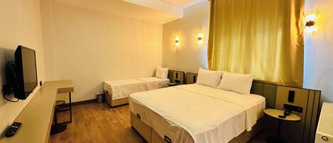 Habitación de hotel con dos camas individuales, una cama doble más grande, un televisor, un escritorio y una mesita pequeña.
