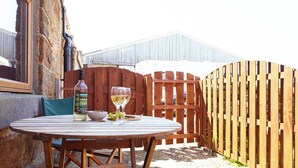 A wooden table with a bottle of sauvignon blanc and two glasses of wine, set against a stone wall and a wooden fence. - Welcome to our charming holiday cottage with breathtaking views of Whitby Abbey (North Yorkshire)