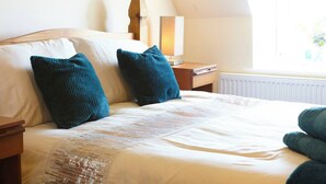 A neatly made bed with two teal pillows, a wooden headboard, a bedside table with a lamp, and a window with a view of greenery. - Welcome to our charming holiday cottage with breathtaking views of Whitby Abbey (North Yorkshire)