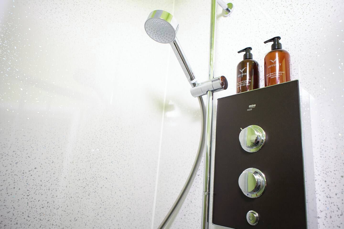 A shower with a handheld showerhead and two bottles of body wash on a control panel.
