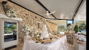 Une réception de mariage avec un gâteau blanc, des compositions florales et un espace extérieur abrité.