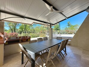 An outdoor patio with a table and chairs, a built-in grill, and a ceiling fan.