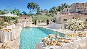 Une réception de mariage organisée au bord de la piscine, avec des tables dressées pour le repas, une piscine aux eaux cristallines et un décor composé d’immeubles et d’arbres.
