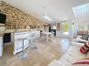 A spacious kitchen with a stone wall, a dining area with white chairs, a white sofa, and a ceiling fan.