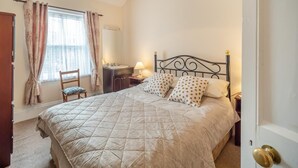 Quarto com cama, escrivaninha, cadeira, mesa de cabeceira e porta.