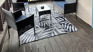 En overdækket terrasse med fletningsmøbler, et mønstret tæppe og lyskæder.