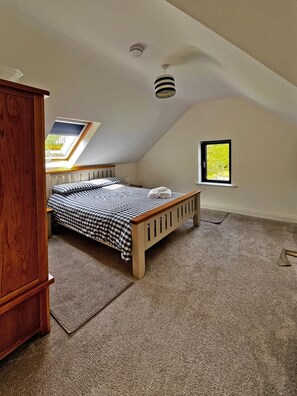 Um quarto com teto inclinado, um claraboia, uma cama com colcha xadrez, uma pequena janela e um radiador.