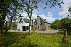 A modern house with a stone extension, surrounded by lush greenery and a clear sky.