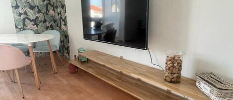 Un salon moderne avec un téléviseur à écran plat fixé au mur, une table basse en bois, une petite table d’appoint et un rideau à motifs floraux.