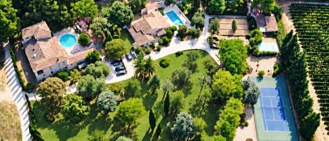 An aerial view of a property with a swimming pool, tennis court, and vineyard.