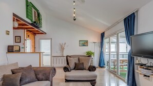 A living room with a sofa, armchair, and television. There is a window with curtains, a radiator, and a plant. - Spacious Apartment w Three Balconies and Parking (Split)