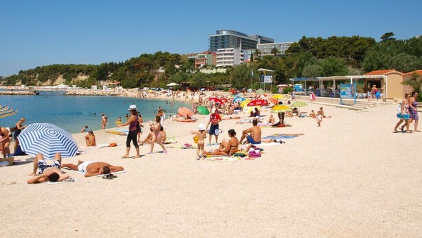 A crowded beach with people sunbathing and swimming, umbrellas, and buildings in the background. - Spacious Apartment w Three Balconies and Parking (Split)