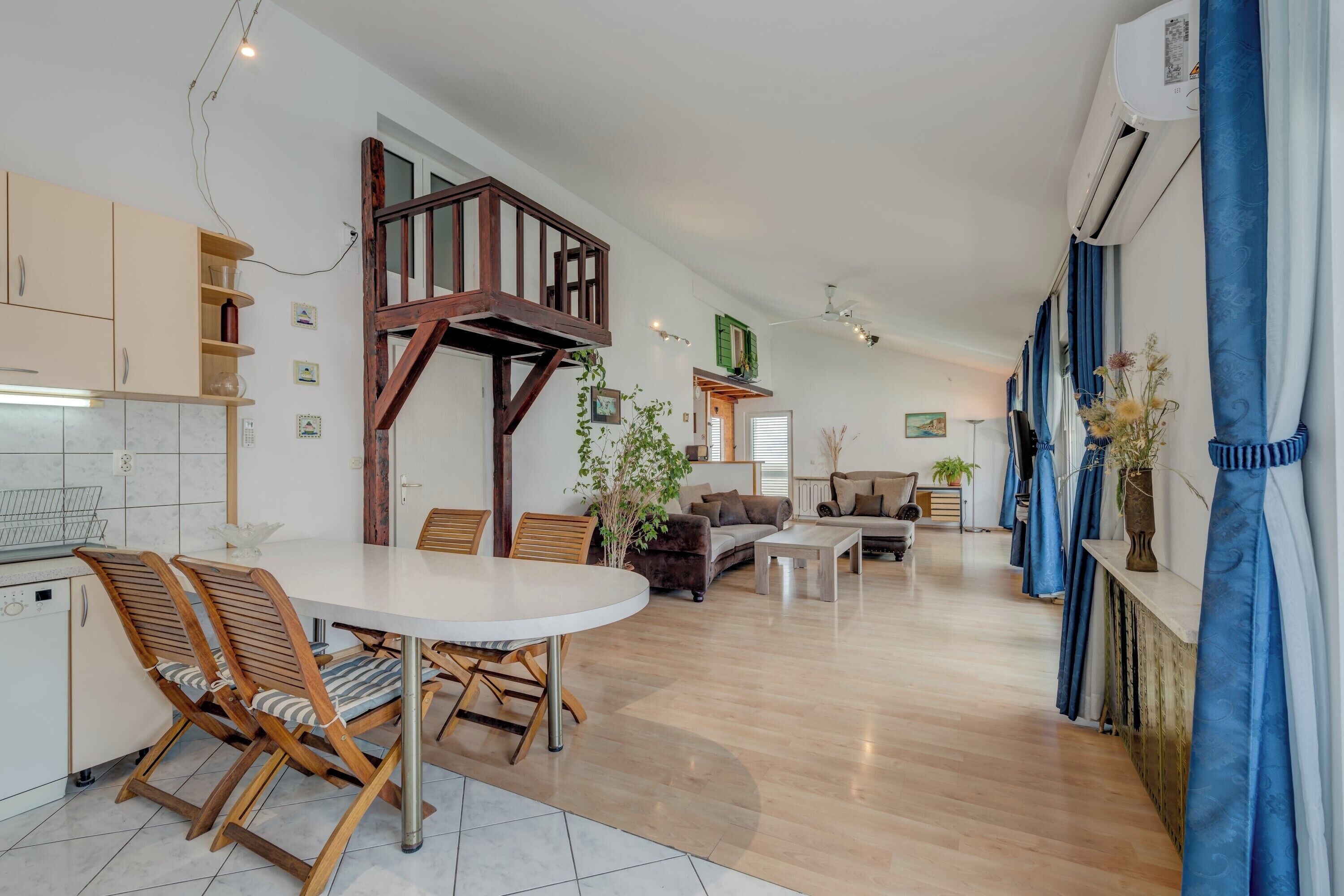 A modern kitchen with white cabinets, a dining table with chairs, a staircase, and a living area with sofas and a coffee table.