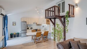 A modern kitchen with white cabinets, a dining area with wooden chairs, and a loft bedroom with a wooden staircase. - Spacious Apartment w Three Balconies and Parking (Split)