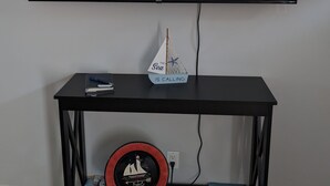 A flat-screen TV mounted on a wall with the text "Hisense · Roku TV" displayed. Below the TV, there is a black TV stand with a small model ship and a book. - "Come Sail Away"
A charming place in Canandaigua designed with a sailing theme.  (Canandaigua)