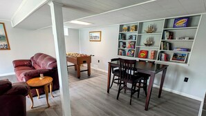 A spacious living room with a wooden floor, a red leather sofa, a wooden coffee table, and a dining table with chairs. There is a bookshelf with various books and decorative items. - "Come Sail Away"
A charming place in Canandaigua designed with a sailing theme.  (Canandaigua)