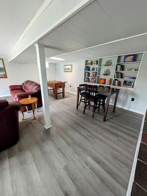 A spacious living room with a wooden floor, a red leather sofa, a wooden coffee table, and a dining table with chairs. There is a bookshelf with various books and decorative items. - "Come Sail Away"
A charming place in Canandaigua designed with a sailing theme.  (Canandaigua)