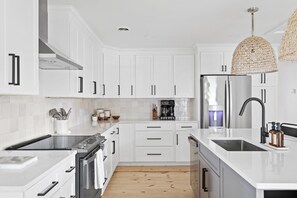 A modern kitchen with white cabinetry, stainless steel appliances, and a wooden floor. - WALK TO THE BEACH!!! Entire 5 bedroom home + game room & fenced in grilling area (Carolina Beach)