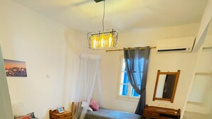 Hotellihuone, jossa on kaksi sänkyä, yöpöytä, peili, riippuvalaisin ja ikkuna, jossa on verhot.