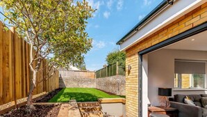 A modern house with a brick exterior, a wooden fence, a well-maintained lawn, and a patio area with outdoor furniture. - Great Value and Something Special (Margate)