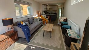 A modern living room with a sofa, coffee table, and a dining area with a kitchen in the background. - Great Value and Something Special (Margate)