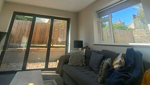 A modern living room with a skylight, a sofa, a coffee table, and a view of the backyard through large sliding doors. - Great Value and Something Special (Margate)