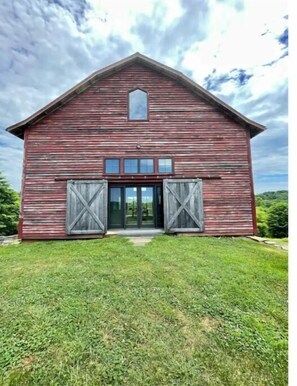 Rustic barn with a central entrance and large doors, set amidst a well-manicured lawn.