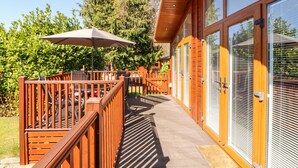 A wooden deck with outdoor seating, a covered patio area, and large windows with blinds.