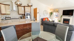 A modern kitchen with stainless steel appliances, a dining area with a glass table, and a living room with a sofa and fireplace.