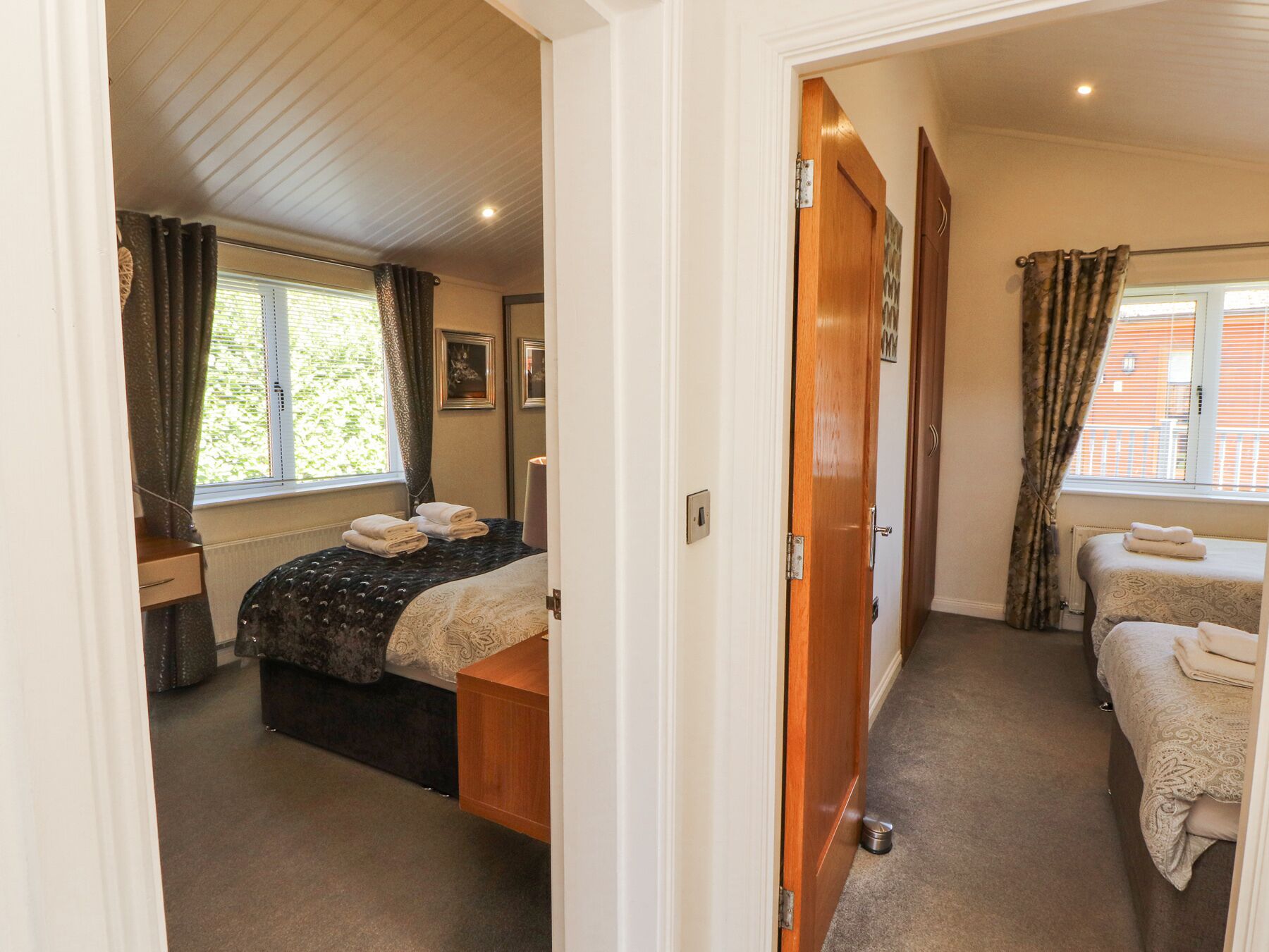 Een hotelkamer met een bed, nachtkastje, raam met gordijnen en een deur naar een andere kamer.