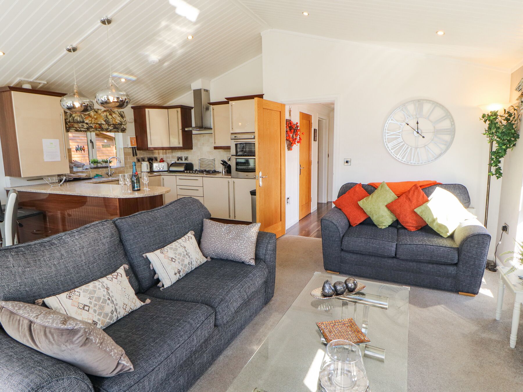 A modern living room with two sofas, a glass coffee table, and a kitchen in the background.