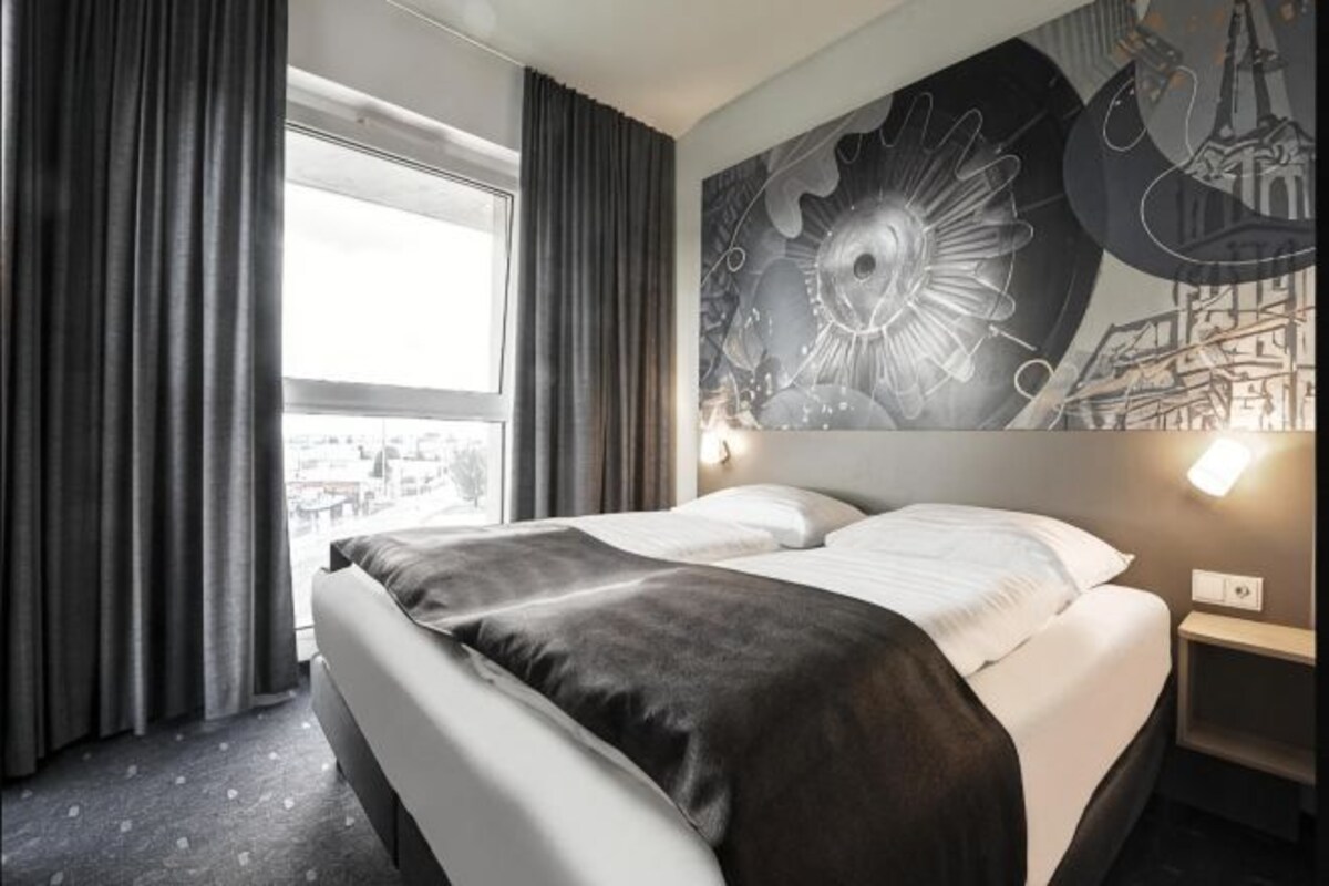 Habitación de hotel con una cama grande, vista panorámica de la ciudad y un mural en la pared.