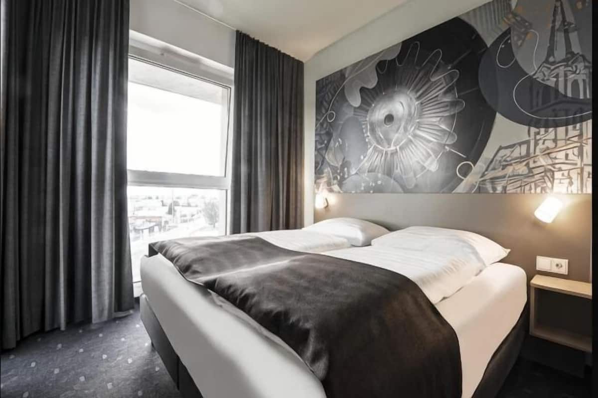Habitación de hotel con una cama grande, vista panorámica de la ciudad y un mural en la pared.