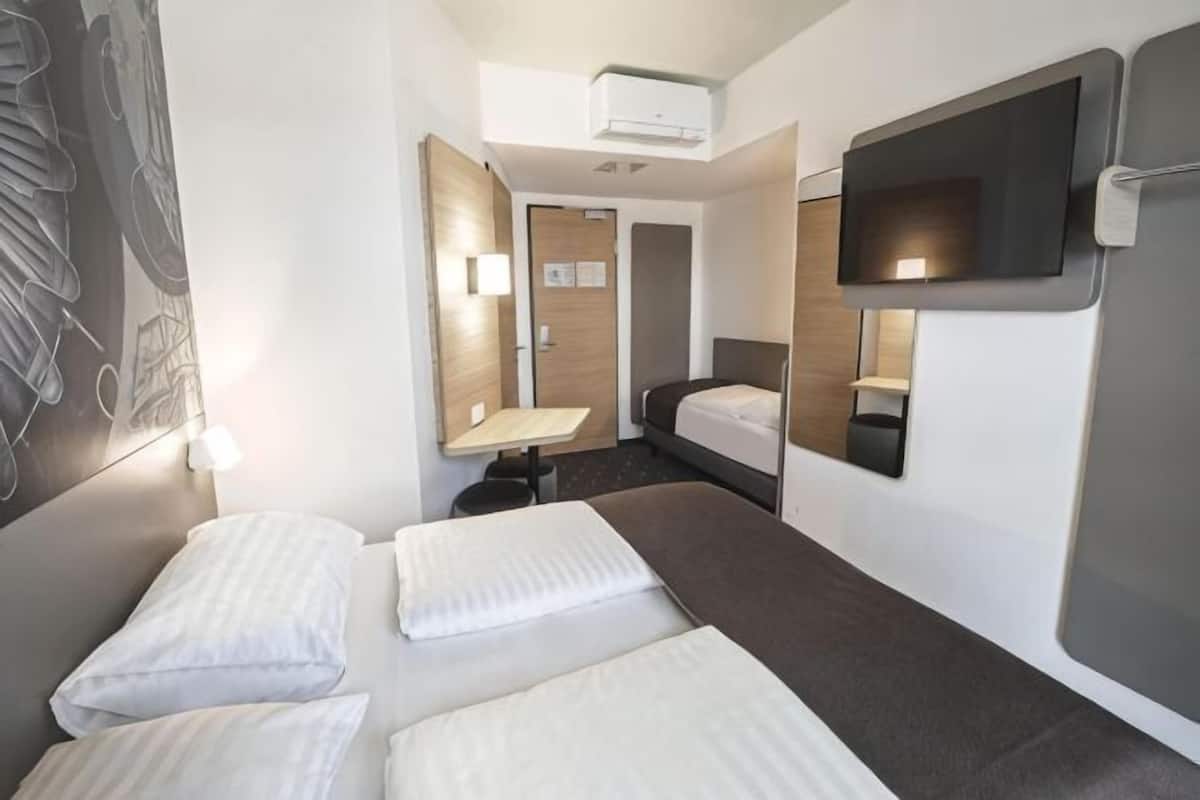 Habitación de hotel con cama, escritorio, silla, televisor y espejo.