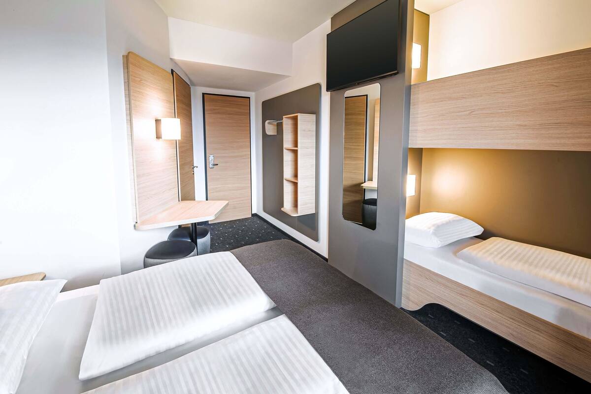 Una habitación de hotel con dos camas, una mesita, una silla, un espejo y un televisor.